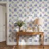 Azulejo wallpaper with bookish tiles behind a carved wooden console table with a linen lamp