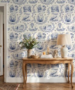 Blue toile wallpaper behind a carved wooden console table with a linen lamp