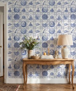Delft tile wallpaper with bookish medallions behind a carved wooden console table with a linen lamp