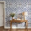Portuguese tile wallpaper with classic blue azulejos behind a carved wooden console table with a linen lamp