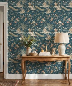 Teal chinoiserie menagerie wallpaper behind a carved wooden console table with a linen lamp